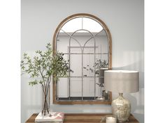 a mirror sitting on top of a wooden table next to a lamp and potted plant