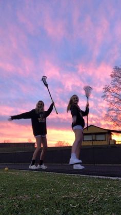 two girls in black shirts and white shorts are playing with brooms while the sun is setting