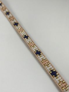 a gold and white bracelet with blue beads on it's end, sitting on a table