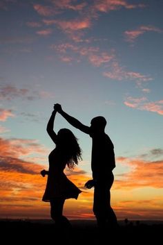 two people standing in front of a sunset with one holding the other's hand