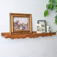 a shelf with two pictures on it and a framed painting hanging above the shelf, next to a potted plant