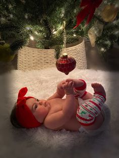 a baby laying on its back in front of a christmas tree wearing a red hat