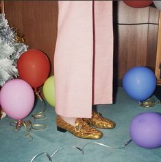 a person wearing gold shoes standing in front of balloons and streamers on the floor