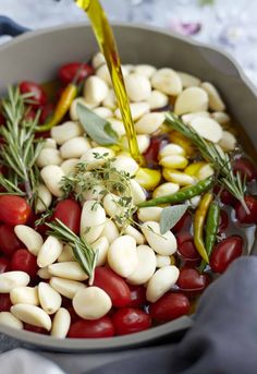 a pot filled with beans, tomatoes and herbs being poured into the pot to make an appetizer