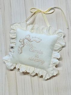 a white pillow hanging on a wall with a ribbon around the edge and an embroidered name