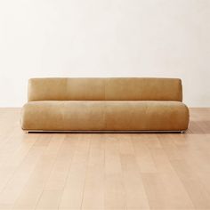 a tan couch sitting on top of a hard wood floor next to a white wall