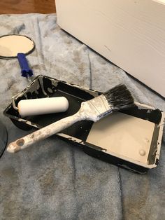 a paintbrush sitting on top of a black tray next to a white and blue brush