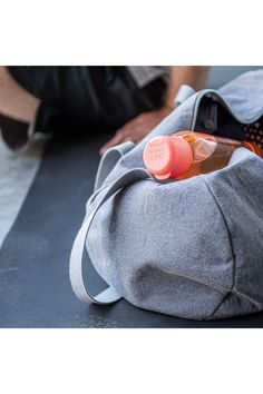 an orange bottle is sitting on top of a gray duffel bag and someone's feet are in the background