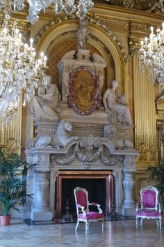 two red chairs sitting in front of a fireplace with chandeliers hanging from the ceiling