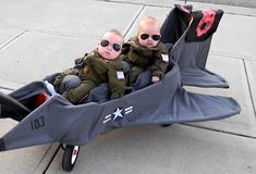 two bald headed babies are sitting in a toy airplane on the sidewalk with sunglasses on