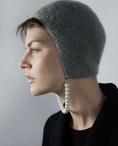 a woman wearing a gray knitted hat with pearls on the brim and earring