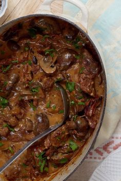 a pot filled with meat and mushrooms covered in gravy next to a spoon