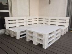 a white bench sitting on top of a wooden floor next to a building with windows