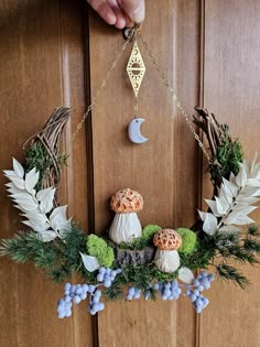 a wreath with mushrooms and greenery hangs on a door handle in front of a person's hand