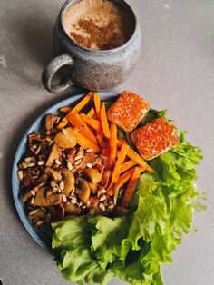 a plate with carrots, mushrooms and lettuce next to a cup of coffee