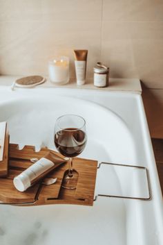 a glass of wine on a tray in a bathtub with other items around it