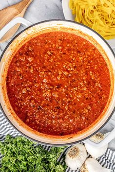 a large pot filled with sauce next to garlic and parsley