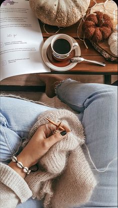 a woman sitting on top of a couch next to a cup of coffee and knitting needles