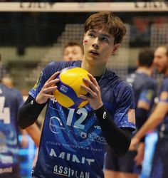 a young man holding a yellow and blue ball in front of other men playing volleyball