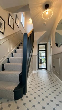 a hallway with stairs and framed pictures on the wall above it, along with tiled flooring