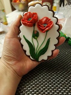 a hand holding a decorated cookie with red flowers on it and green leaves in the middle