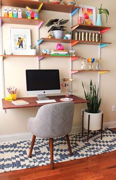 a desk with a computer, chair and plant on it in front of a white wall