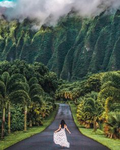 a woman in a white dress is walking down the road with trees on both sides