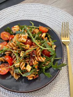 a black plate topped with pasta salad next to a fork