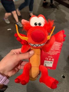 a hand holding a red stuffed animal with big eyes and large teeth on it's face