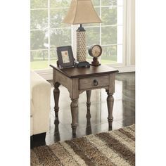 a table with a lamp on top of it next to a couch and rug in front of a window