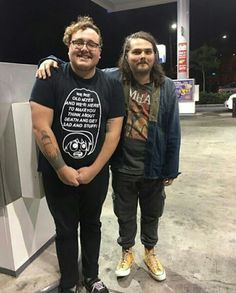 two men standing next to each other in front of a gas station