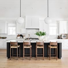 a kitchen with white cabinets and black island in the center is surrounded by stools