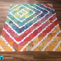 a multicolored quilt is laying on the floor in front of a wooden floor