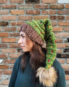 a woman wearing a knitted hat with a fur pom in front of a brick wall