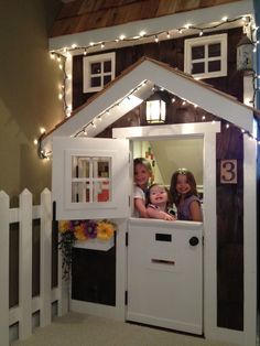 two girls and a boy are in a doll house with lights on the outside wall