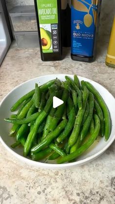 a white bowl filled with green beans on top of a counter next to an avocado oil bottle