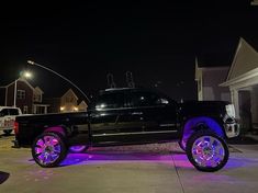 a black truck with purple rims parked in front of a house at night time