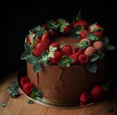 a chocolate cake topped with strawberries and green leaves on top of a wooden table