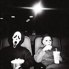 two people sitting in chairs with masks on their faces, one holding a drink and the other eating popcorn