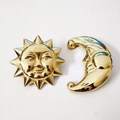 two metal sun and moon brooches on a white surface, one has a face