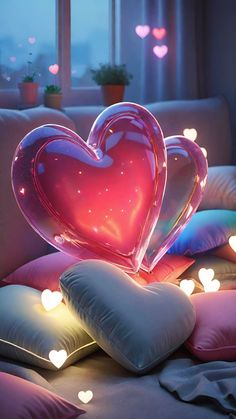 two heart shaped pillows sitting on top of a bed in front of a window filled with lights