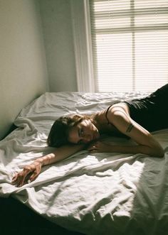 a woman laying on top of a bed next to a window