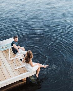 a man and woman sitting on a dock in the water