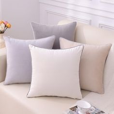 four pillows on a white couch with flowers in the vase next to it and magazines