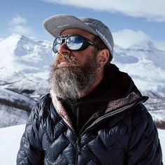 a man with a beard wearing sunglasses and a hat on top of snow covered ground