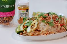 a white plate topped with noodles and vegetables next to a jar of peanut butter sauce