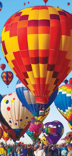 many colorful hot air balloons in the sky with people looking at them and taking pictures