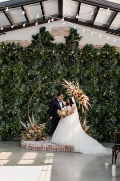 a bride and groom standing in front of a wall with greenery on it at their wedding