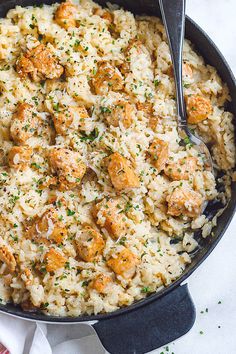 a skillet filled with chicken and rice on top of a white table cloth next to a fork