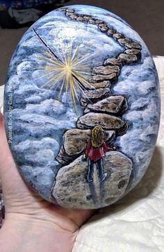 a hand holding a painted rock with a person standing on the rocks and stars above it